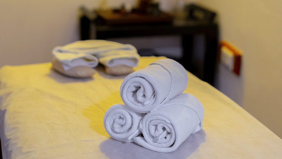 A neatly prepared therapy bed with rolled white towels and soft ambient lighting - Johnson Lodge & Spa, Manali