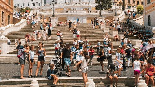 A public square with a fountain, steps, and many people walking or sitting.