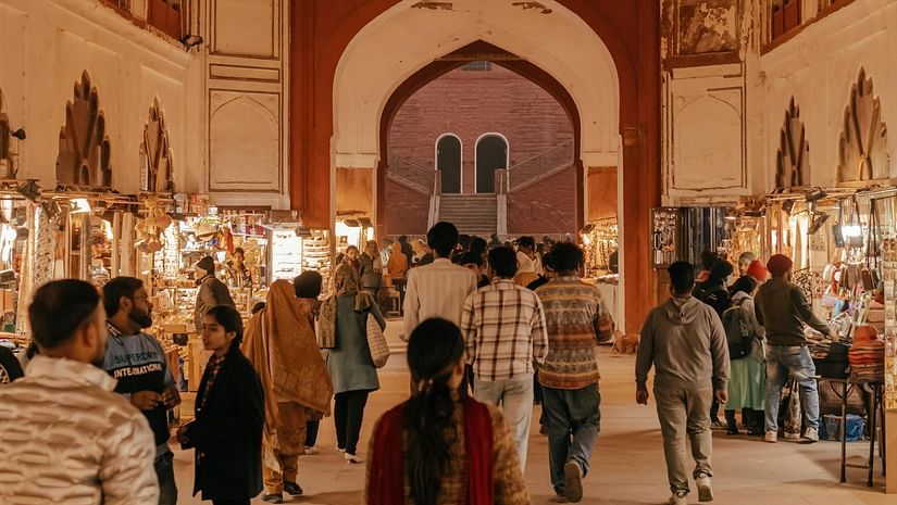 A view of people walking in a market with shops lined on both sides and a gateway in the backdrop