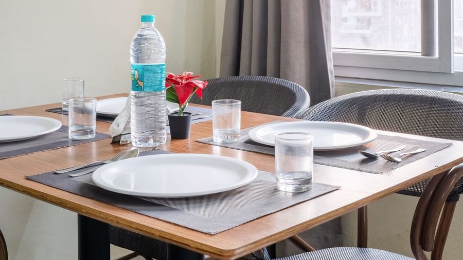 A close-up of a dining table set with bottled water and plates, beside a window.