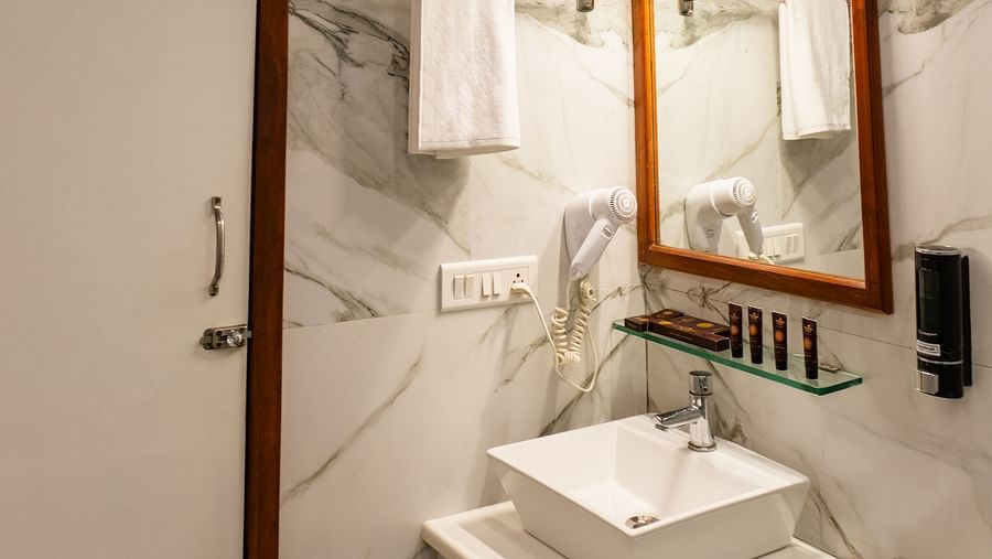 Bathroom of Lawn View Tent Room at The Grand Legacy Resort and Spa featuring a sleek sink, marble walls, a stylish mirror, a patterned ceiling, and neatly arranged towels.