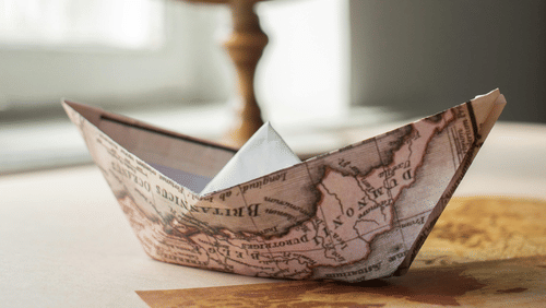 A paper boat made from a map, with a globe in the background