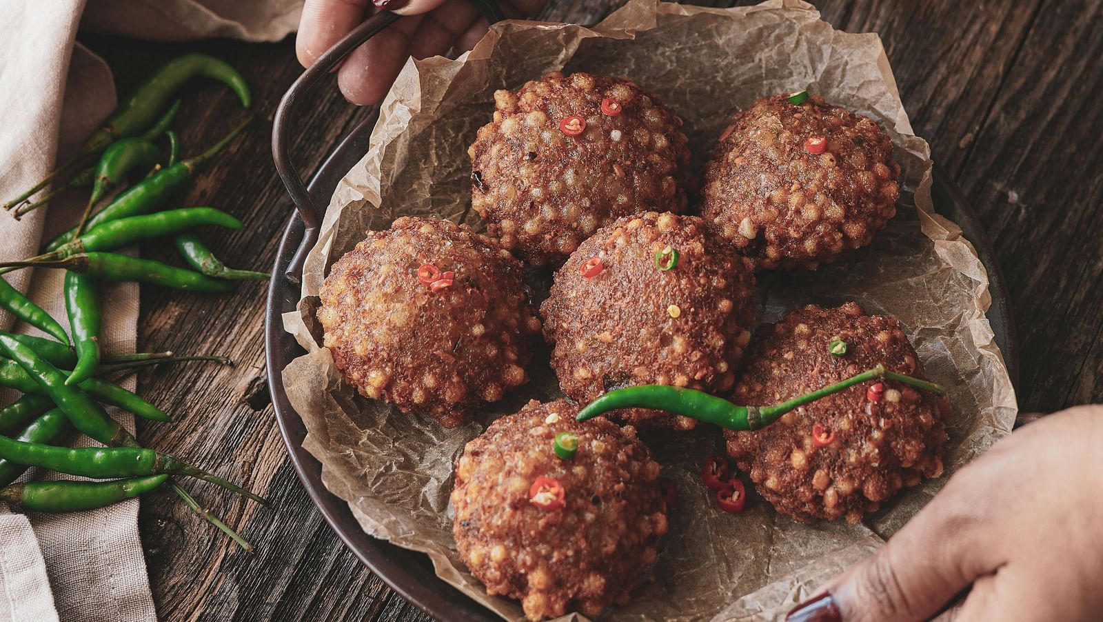A woman placing a tray of sabudana vada on a table.