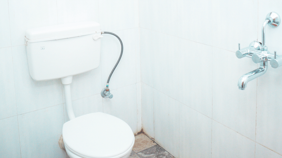 A brightly lit washroom with a commode and a geyser above it 
