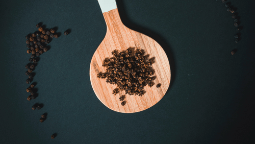 An aerial view of black pepper kept on a wooden spoon.
