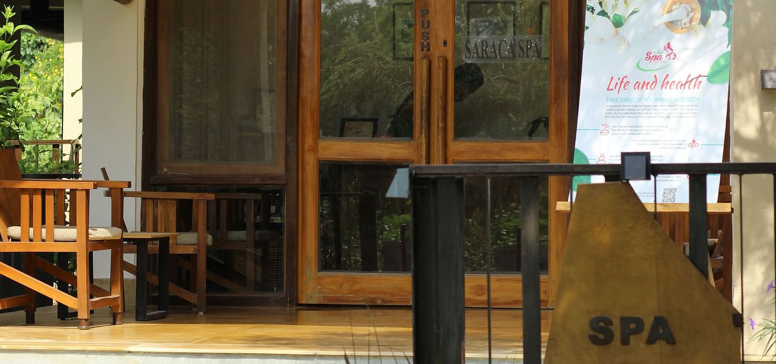 Entrance to the spa at Saraca Resort & Spa Corbett with large glass doors with wooden panels and greenery surrounding the building