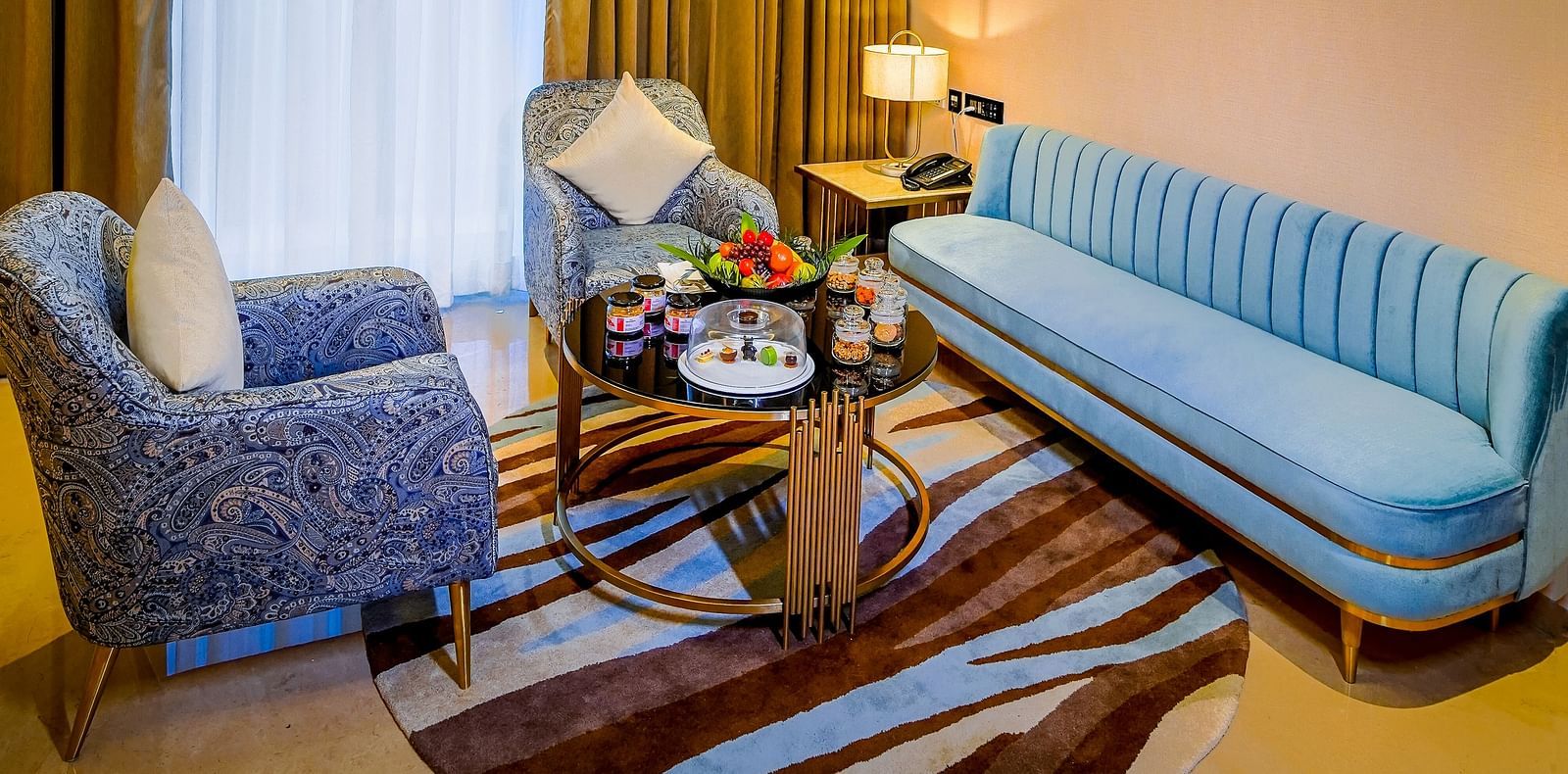 An image of a living room in Grand Velammal Suite with a large blue couch and a sofa placed around a coffee table