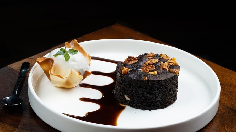 A dessert, possibly a chocolate cake, garnished with cream and berries on a white plate at The Qualia Resort Club & Brewery, Udaipur.