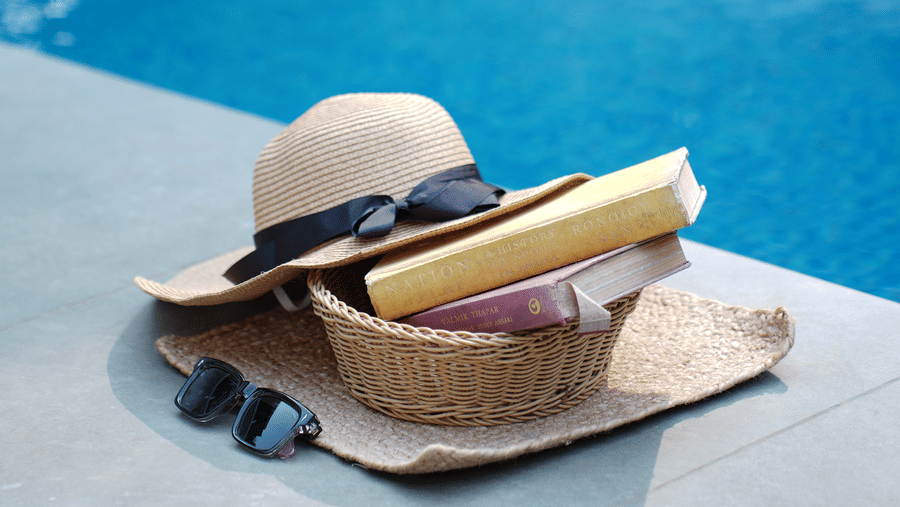 A sun hat, sunglasses, and a basket sit on the edge of a swimming pool at Bougainvillea, Alibaug.