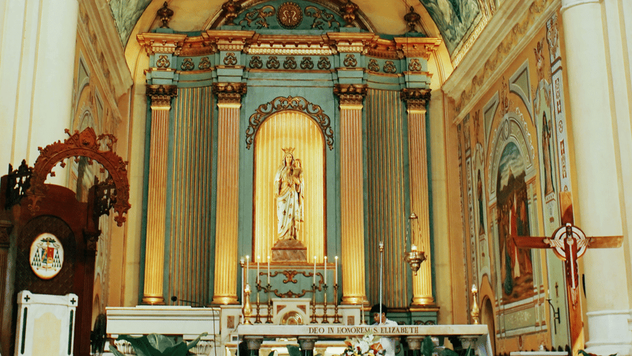 Ornate church interior with painted ceilings, arched columns, and an altar.