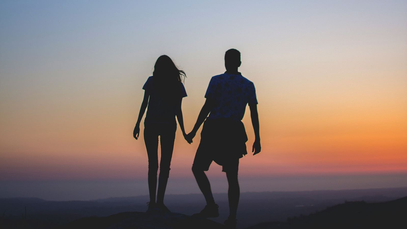 Two people holding hands against a golden sky