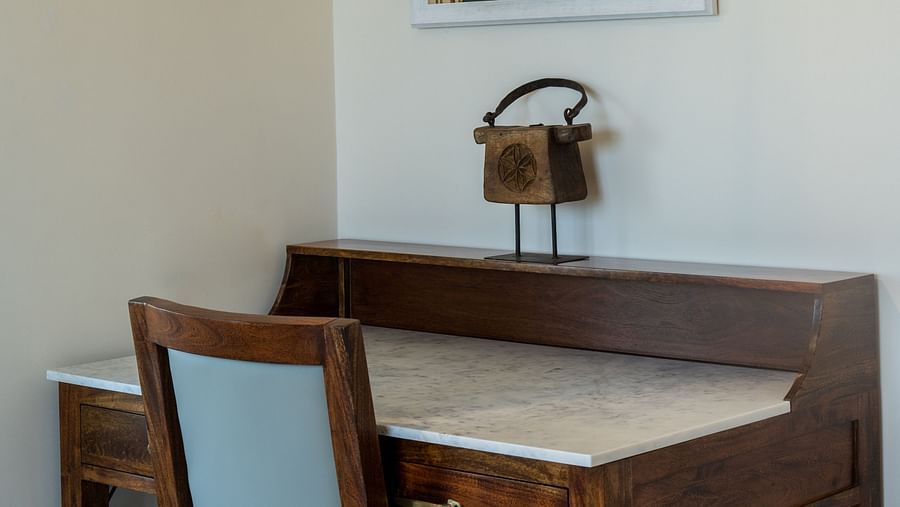 A cosy wooden table and chair placed in front of a wall with a wall-mounted painting - Rajbagh Wellness, Udaipur