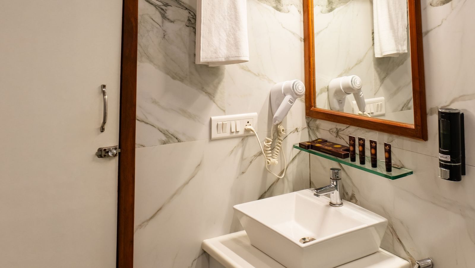 Bathroom of Lawn View Tent Room at The Grand Legacy Resort and Spa featuring a sleek sink, marble walls, a stylish mirror, a patterned ceiling, and neatly arranged towels.