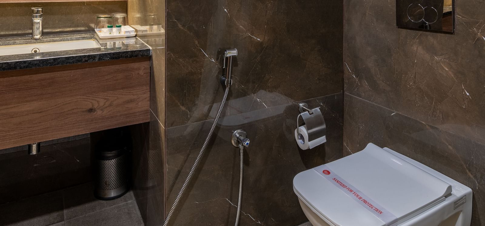 Modern bathroom with wall-mounted toilet and dark-toned tiles at Hotel Highway King, Bilaspur.