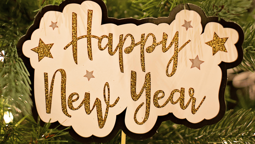 A 'Happy New Year' sign and a clock ornament hang on a decorated Christmas tree.