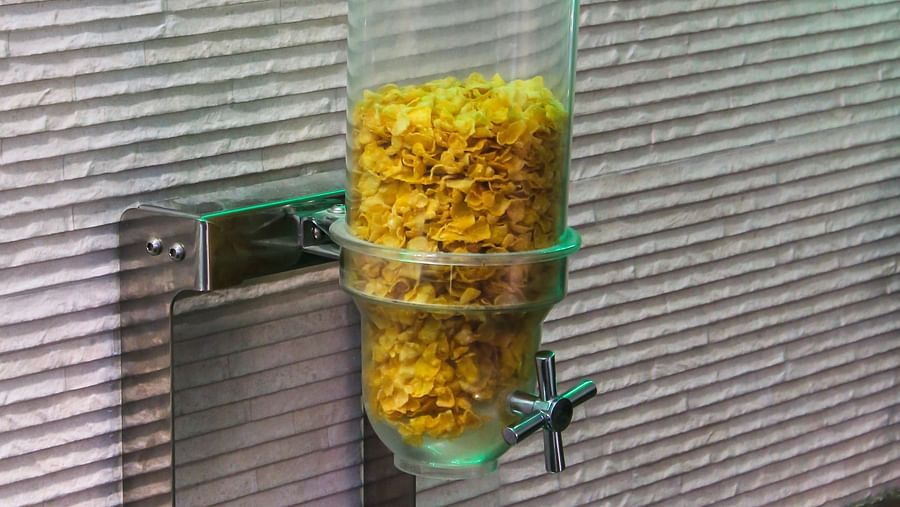 A clear plastic dispenser filled with cereal, mounted on a textured wall with green lighting above. - Hotel Diamond Plaza, Chandigarh.
