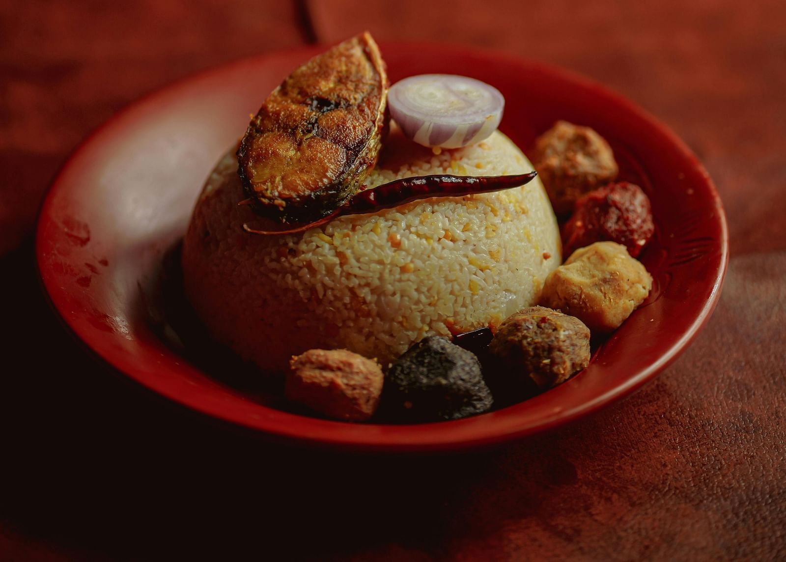 A plate of Bengali Thali food with rice, dal, vegetables, and a small bowl of dessert, on a dark background with bokeh lights.