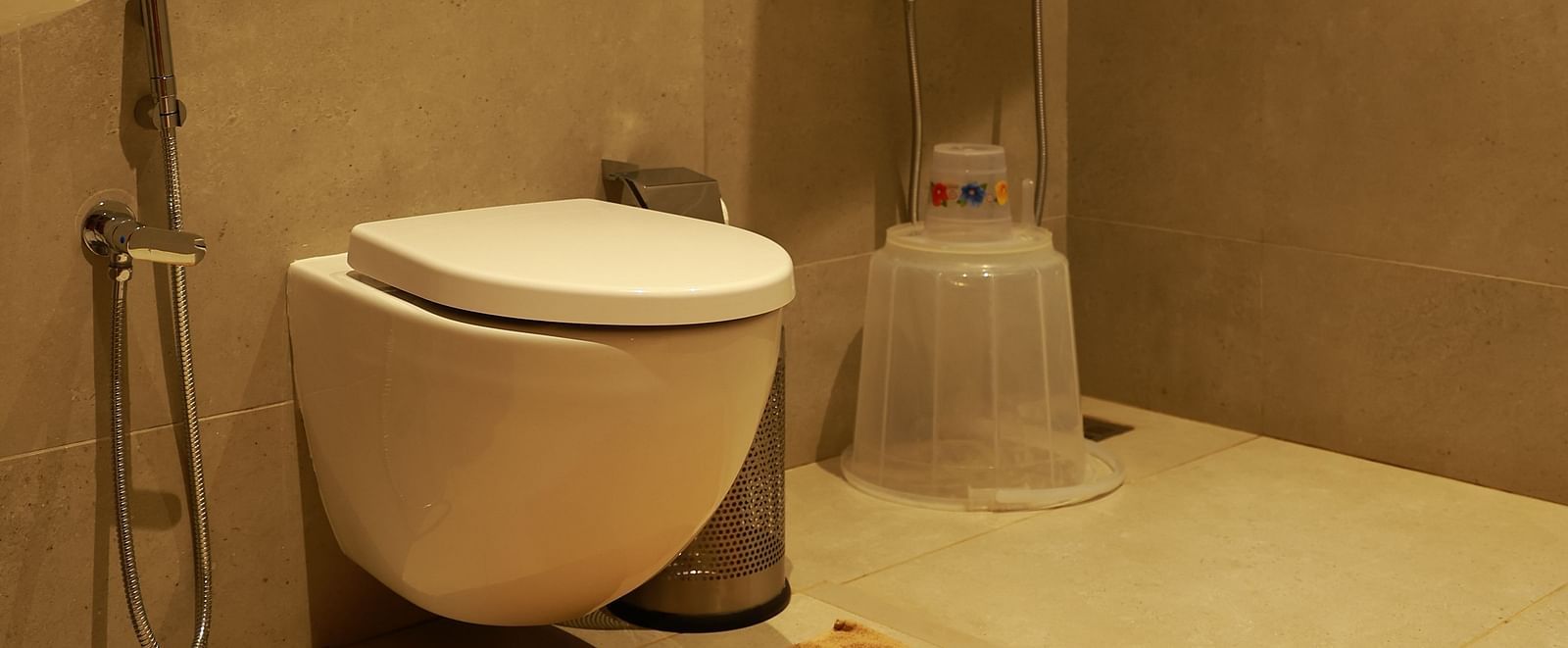A contemporary bathroom at Vaasta Vagamon featuring a wall-mounted toilet, a walk-in shower with a rainfall showerhead, and a bath mat.