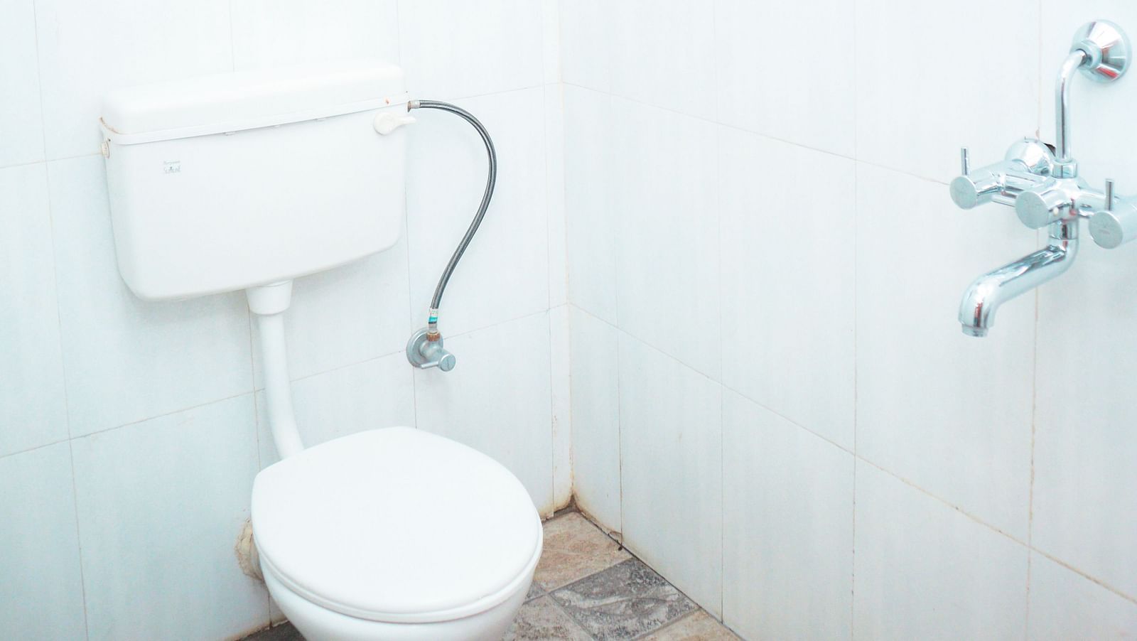 image of a brightly lit washroom with a commode and a geyser above it 