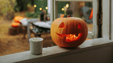 Pumpkin with a carved face placed on a window sill, glowing in the warm afternoon light.