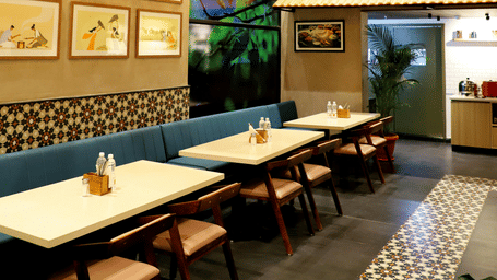 Intimate restaurant nook with framed art, patterned tiles, and a warm timber ceiling.