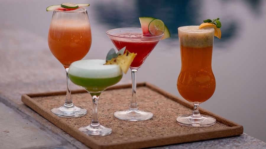 A portrait image of four colorful cocktails placed on a serving plate, with the soft bokeh effect of water reflections from the swimming pool and decorative lights in the background - Crescent Resort, Goa