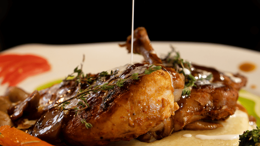 A meat dish kept in a plate featuring sauce being poured from above at Hotel Sonar Bangla, Ajodhya Hills.
