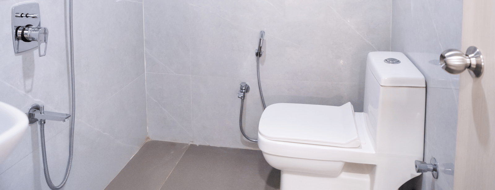 Spacious bathroom with a western toilet and shower area, brightly lit at Sunrise Business Hotel, Hyderabad.