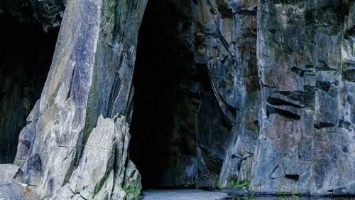 A narrow cave with a pool at the base, surrounded by stone walls.