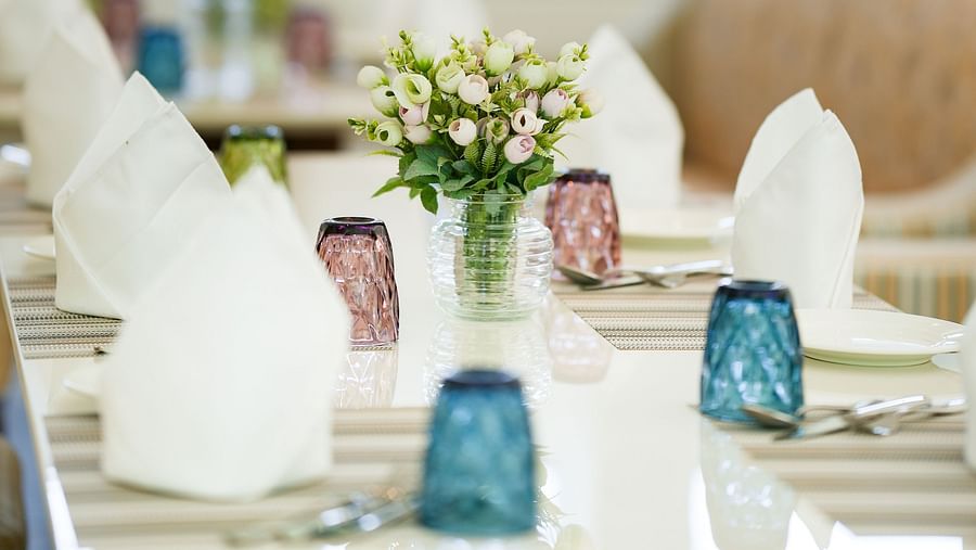 A close-up shot of a table with neatly folded napkins, glasses, and cutlery arranged on it, along with vases of flowers in between - NAMAMI BY ZENQ BANKHANDI