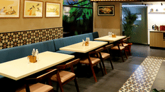 The interior of a casual restaurant or cafe with wooden tables, booth seating, hanging light fixtures, and framed pictures on the walls.