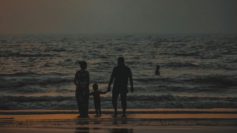Three people stand on a beach at dusk, with narrow lighting creating.