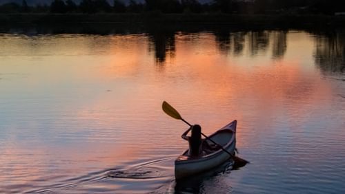 A person kayaking on a river with the sun setting behind it - Ramgarh Bungalows, Nainital.