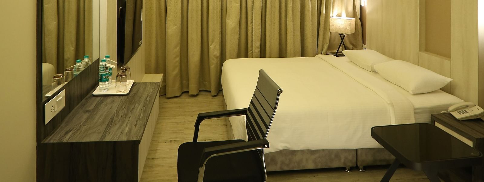 Premium Room shown with a king size bed, desk, chair, and mirror, illuminated by warm lighting - TGI SPS Grand, Coimbatore