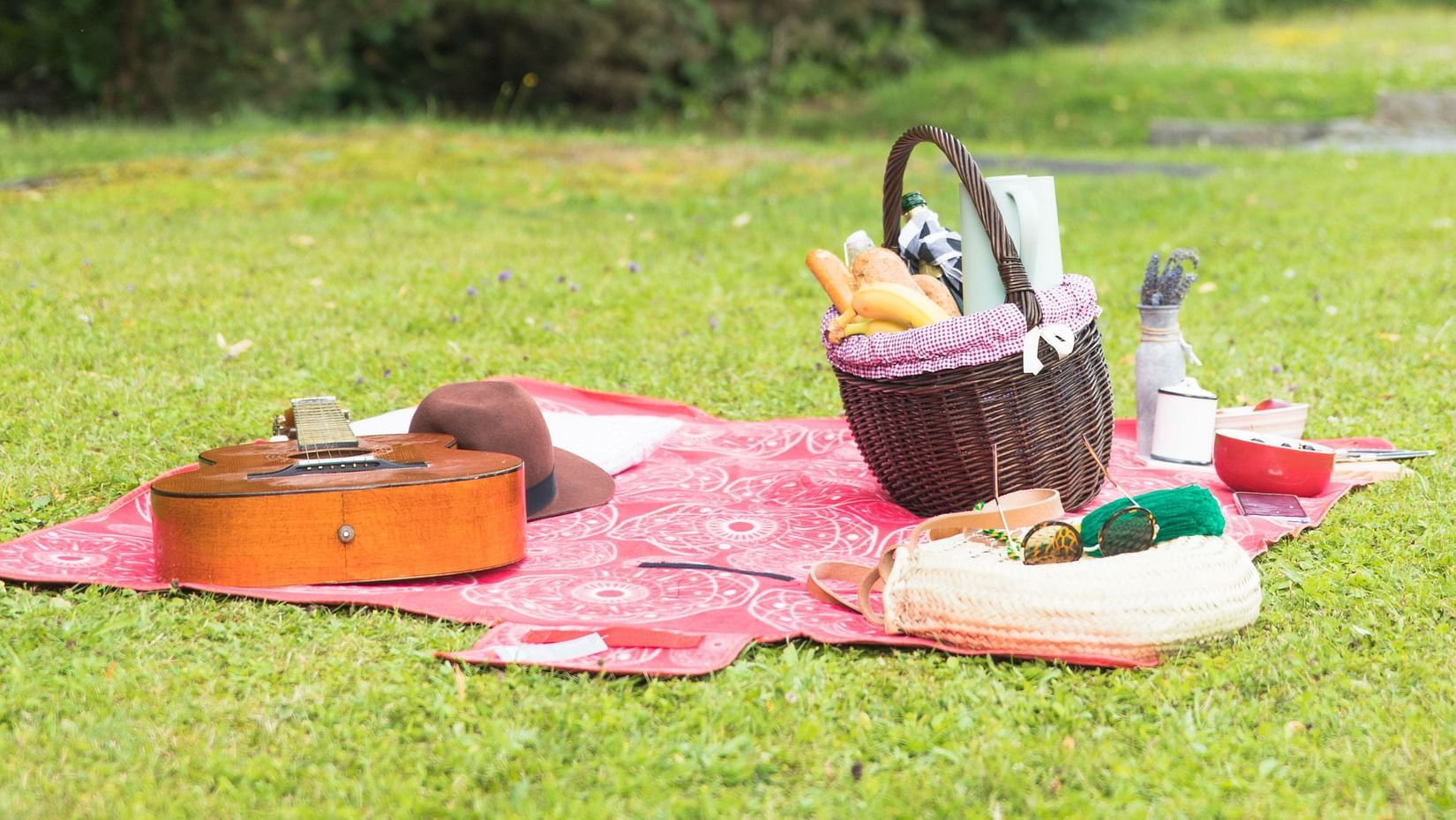 A picnic basket filled with food and personal accessories, shot with green lushy backdrops.