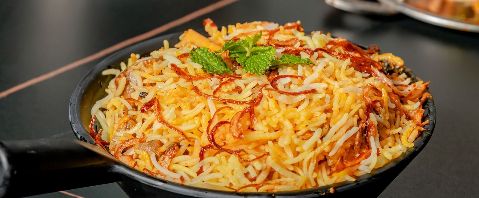Bowl of biryani or pulao on a black table next to a small dish | Pravasa Hotel, Vijayapura