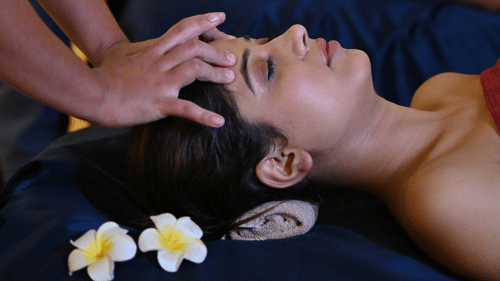 Couple receiving relaxing head massages at a spa, lying side by side on massage beds with flowers placed nearby, creating a calming and luxurious wellness atmosphere - Ananta Spa and Resort, Pushkar.