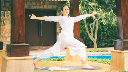 Woman practicing yoga in an open-air wooden pavilion with tiled roofing, surrounded by greenery, creating a serene and peaceful atmosphere - Ananta Spa and Resort, Pushkar.