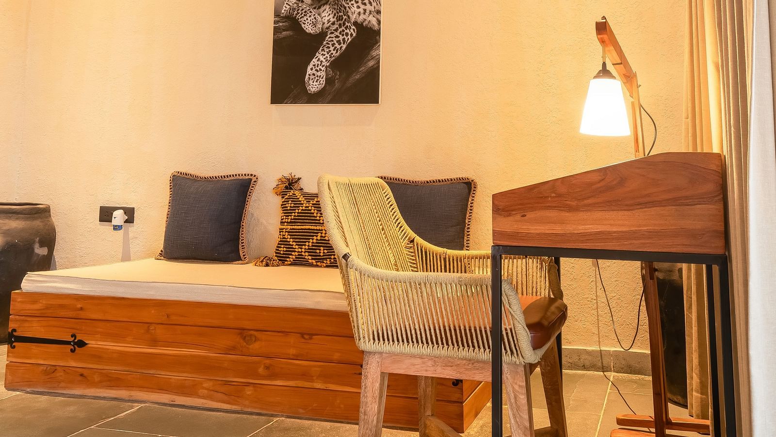 An image of a living area featuring a work desk and chair, an AC, a sofa, and some decorative elements at Kurja Jawai