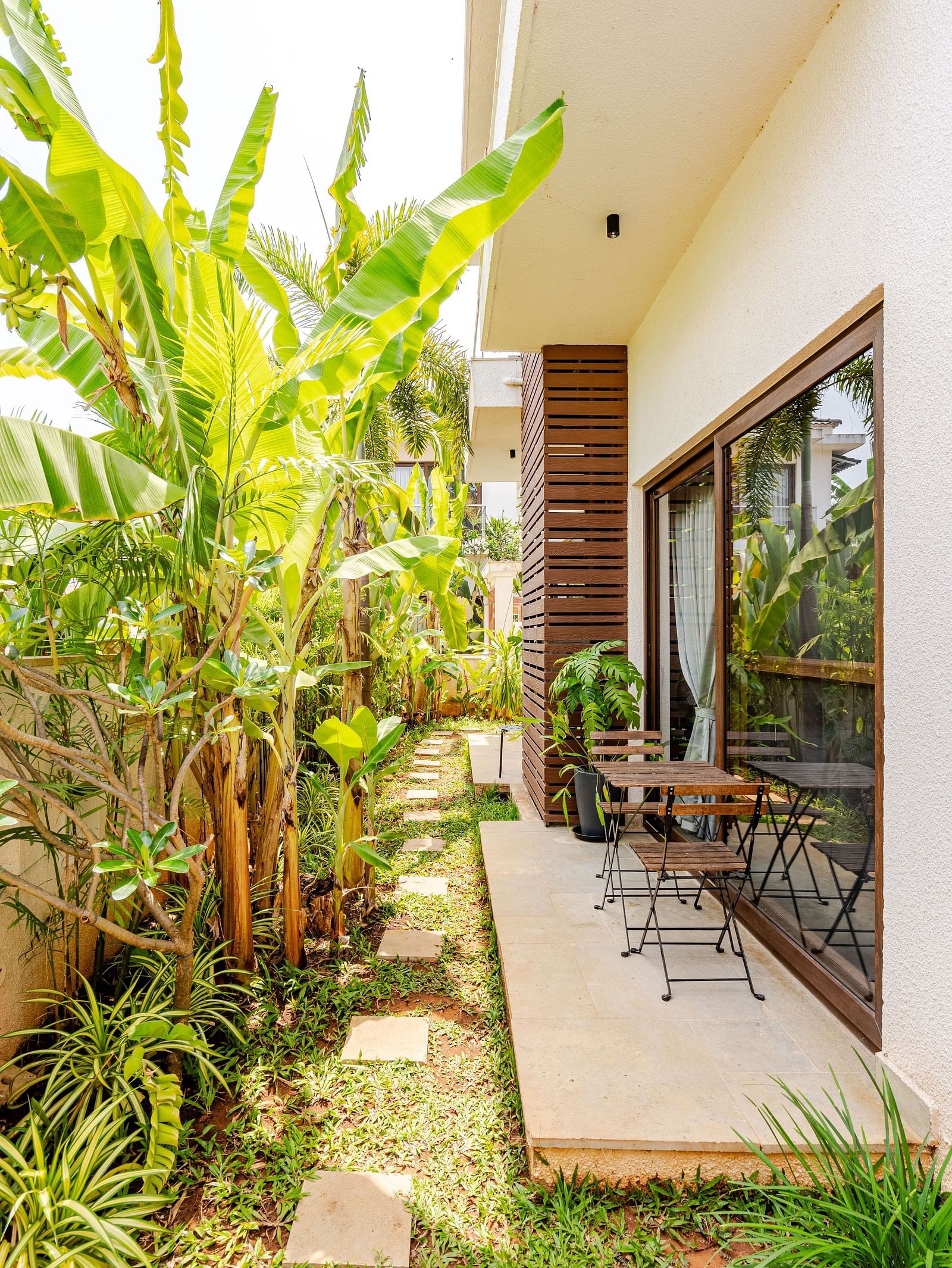 Outdoor pathway at Lindsay Manor with a garden on one side and a glass door leading into a room on the other.