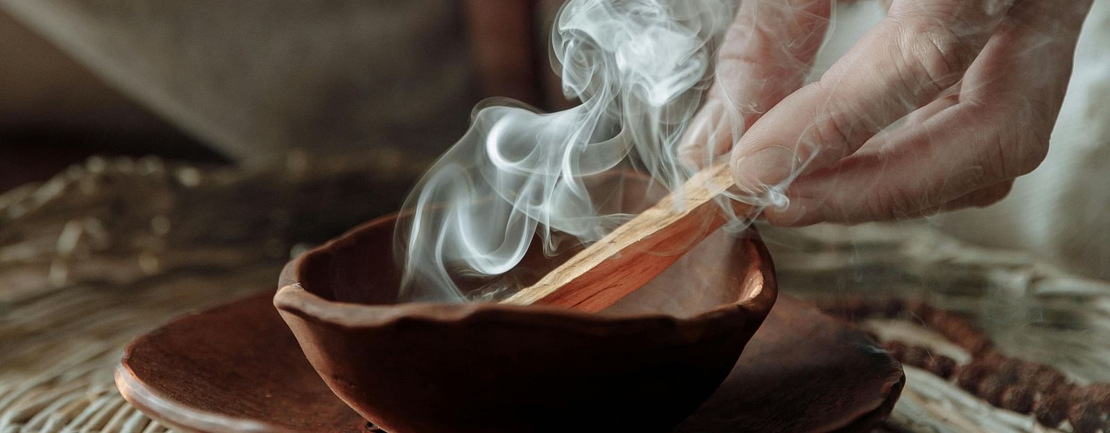 A person sitting on a huge mat burning incense sticks into a bowl.