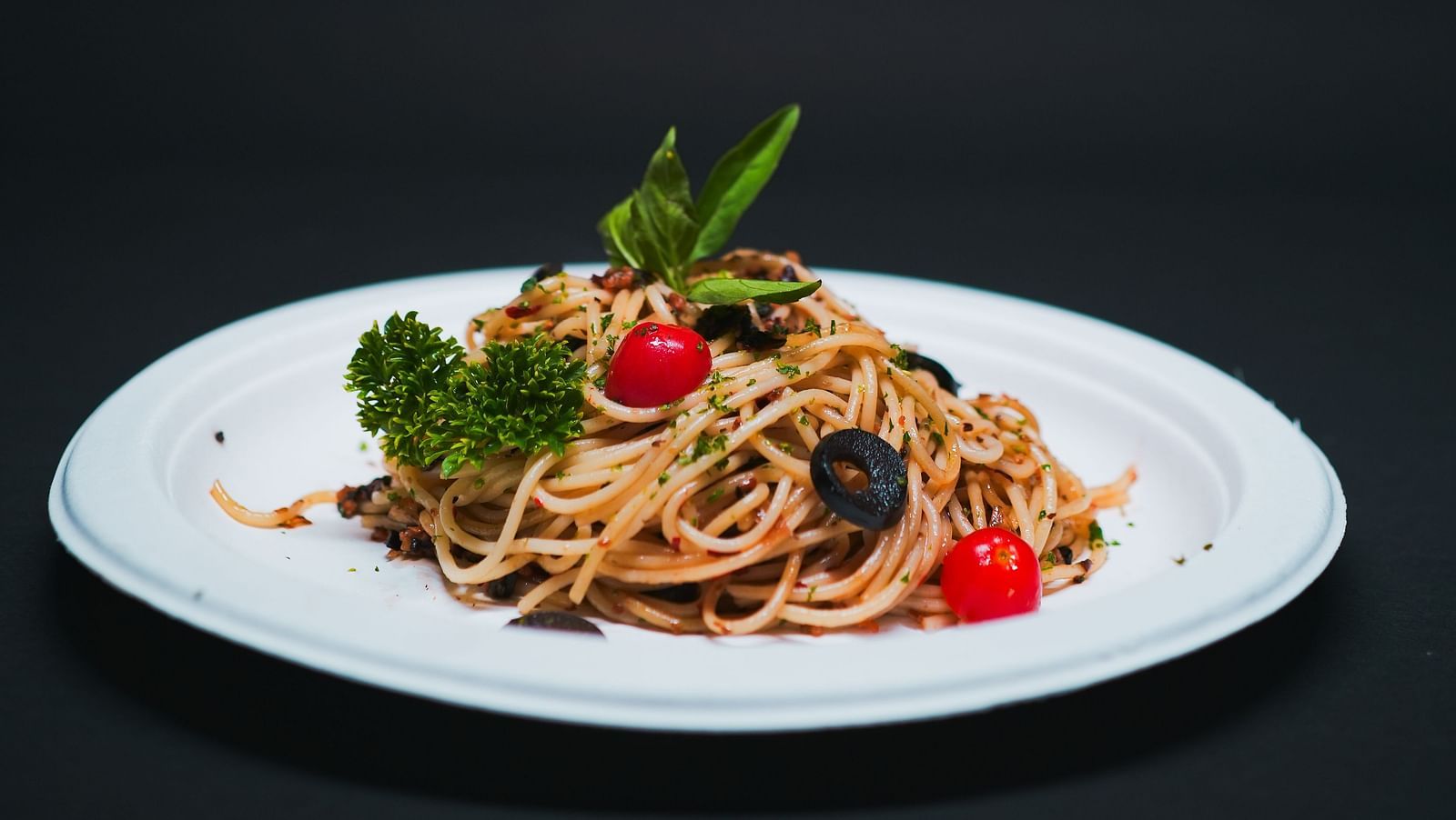 A plate of spaghetti garnished with olives, cherry tomatoes, and herbs, elegantly presented at D Café in Dip Holidays.