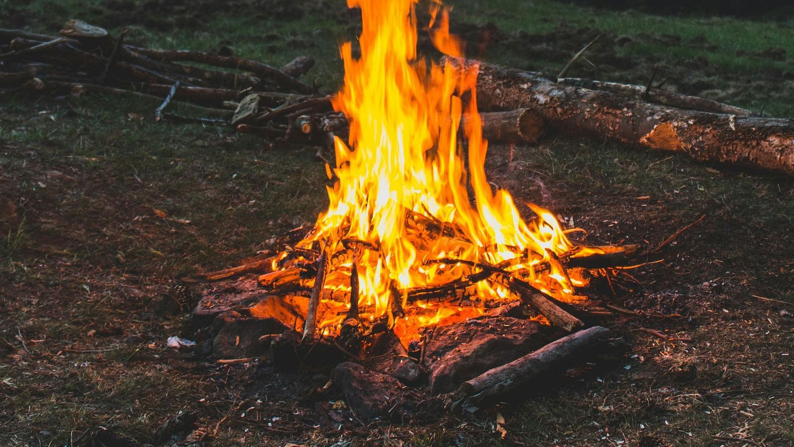 A campfire burns brightly in a mountain landscape at dusk.