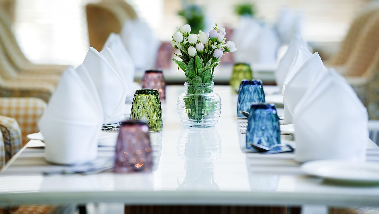 A view of a table featuring neatly arranged napkins, glasses, and cutlery, with flower vases placed in between - NAMAMI BY ZENQ BANKHANDI