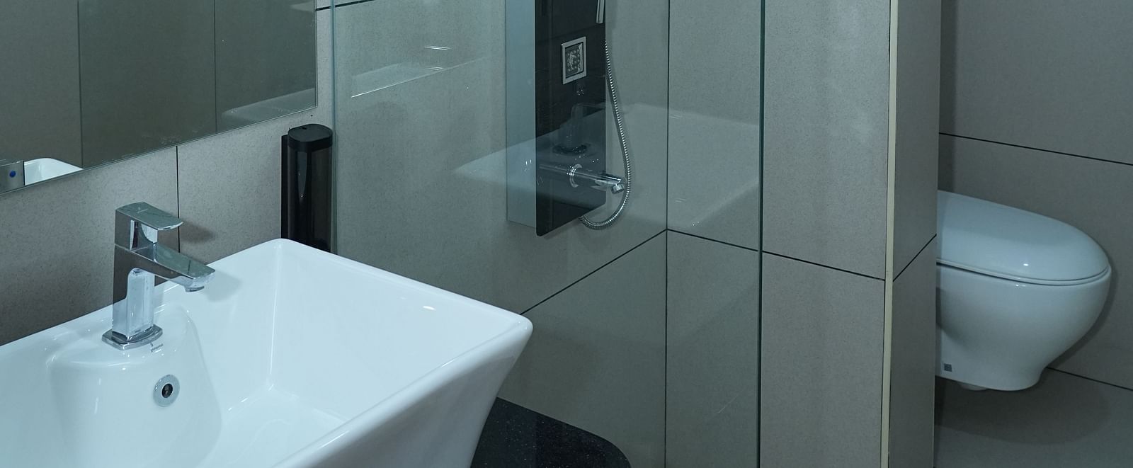 full view image of the bathroom featuring a wash basin along with a shower cubical and a commode separated by a glass partition - Hotel Grand Sigma