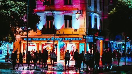 Building lit up at night with reflections on a wet street, creating a vibrant, colourful scene.