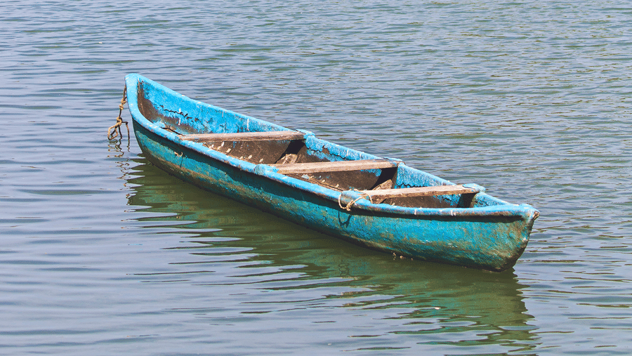 Small wooden boat floating on calm river water with greenery and trees along the Suvarna Backwater at Paradise Lagoon Resort, Udupi.