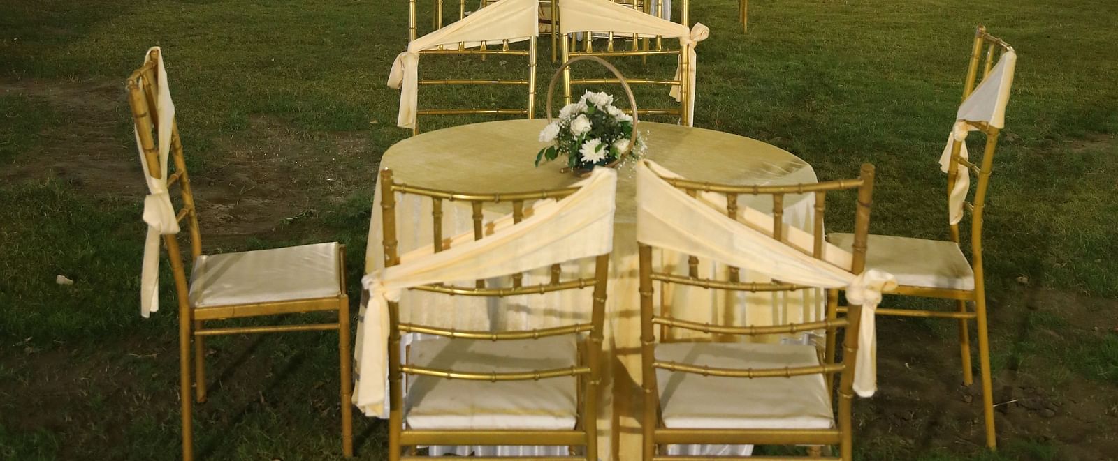Close-up of a banquet table and chairs under decorative lights on the lawn at Tisya Farms, Gurgaon.