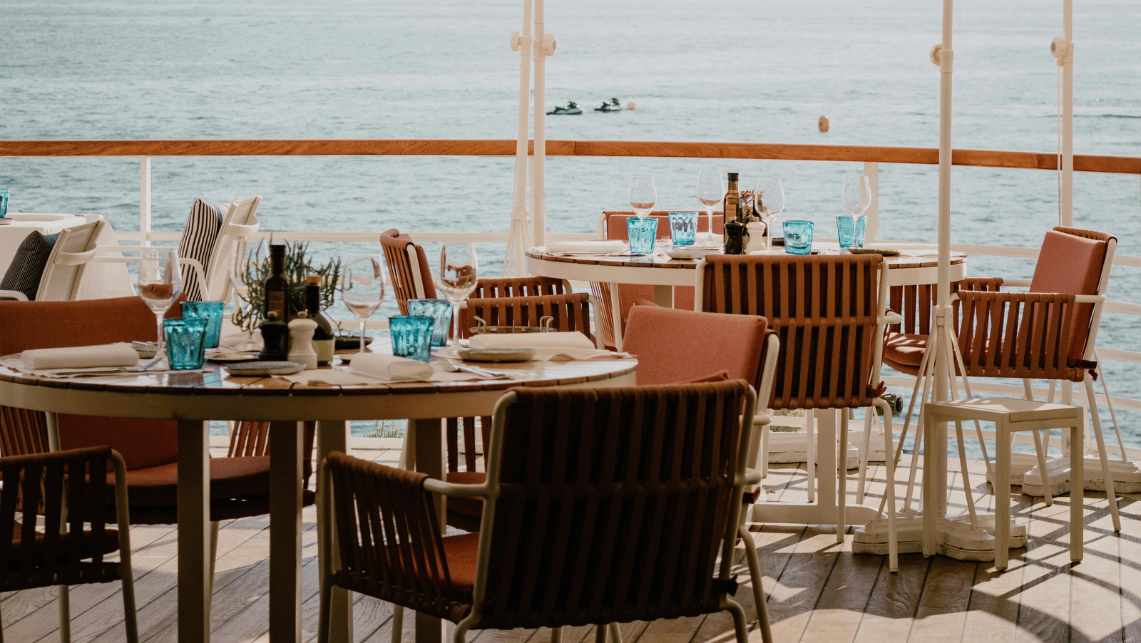 An outdoor dining table set with chairs featuring a distant view of the ocean at Trishvam Palolem Beach Resort, Goa.