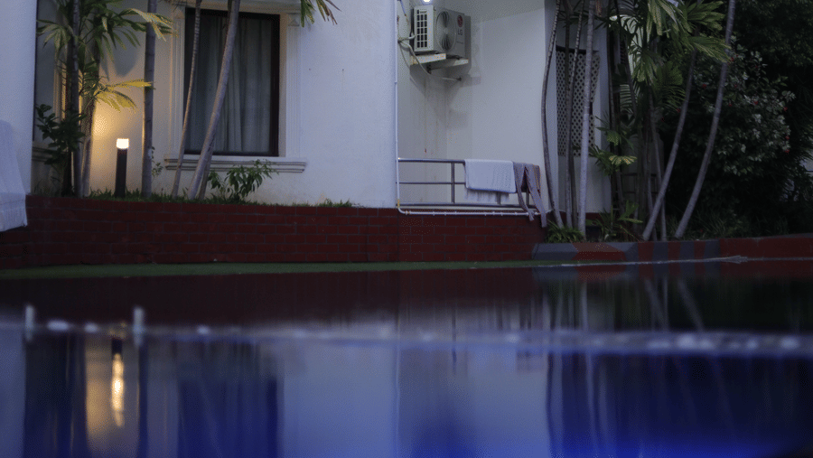 Exterior of Ilara Hotels & Spa, OMR, Chennai illuminated exterior by dusk, reflecting in the tranquil waters of the swimming pool.